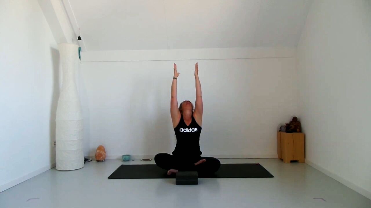 Caroline van den Ende zit op haar yogamat en strekt beide armen omhoog
